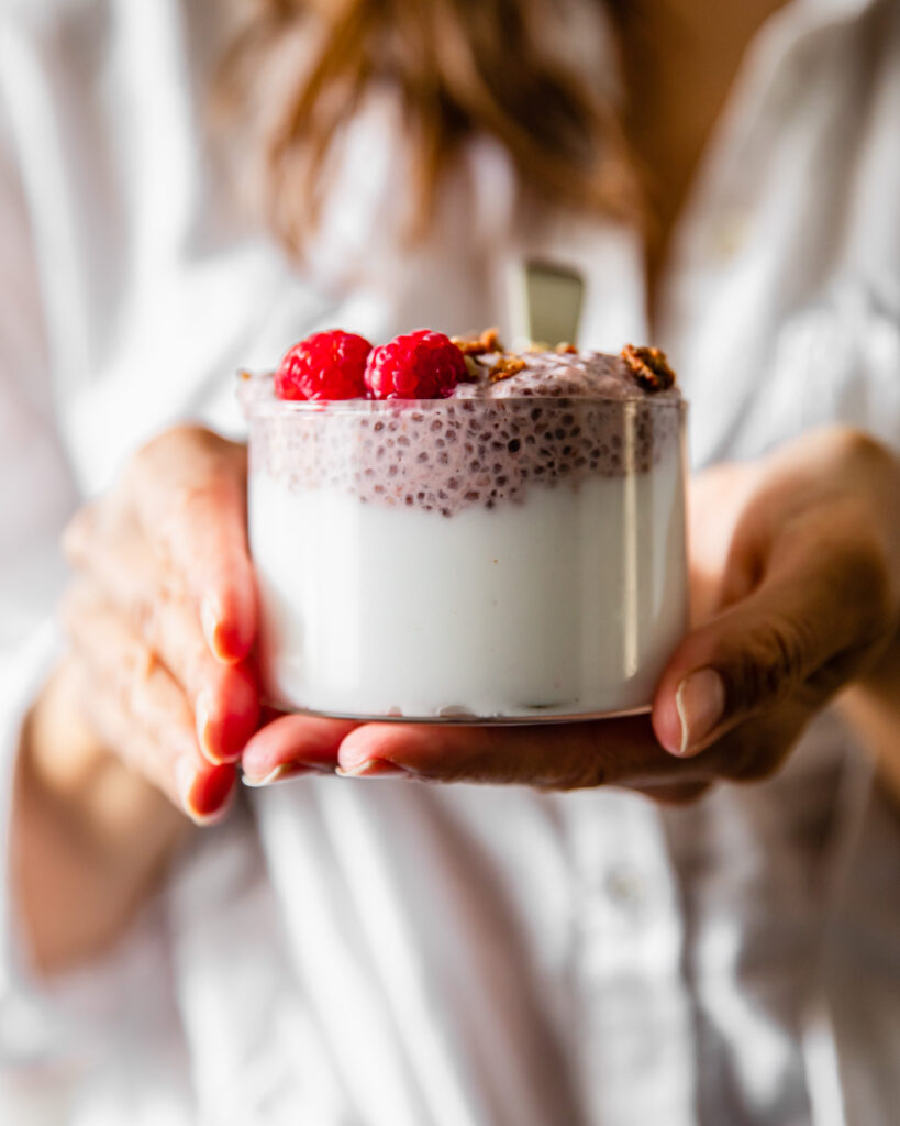 Woman holding a chia seed pudding in clear glass.